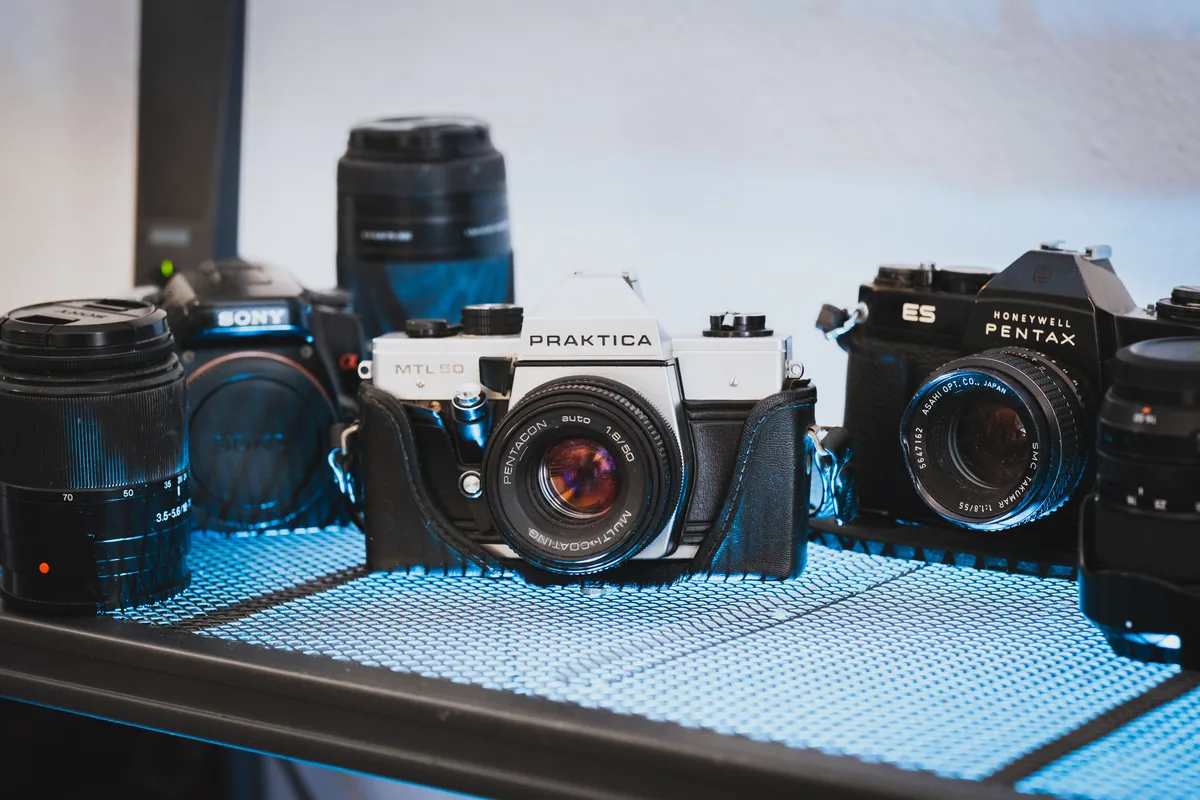 Antonio Vargas’s film cameras on a shelf: a Sony Alpha, a Praktica MTL 50 with a Pentacon 50mm lens, and a Honeywell Pentax ES
