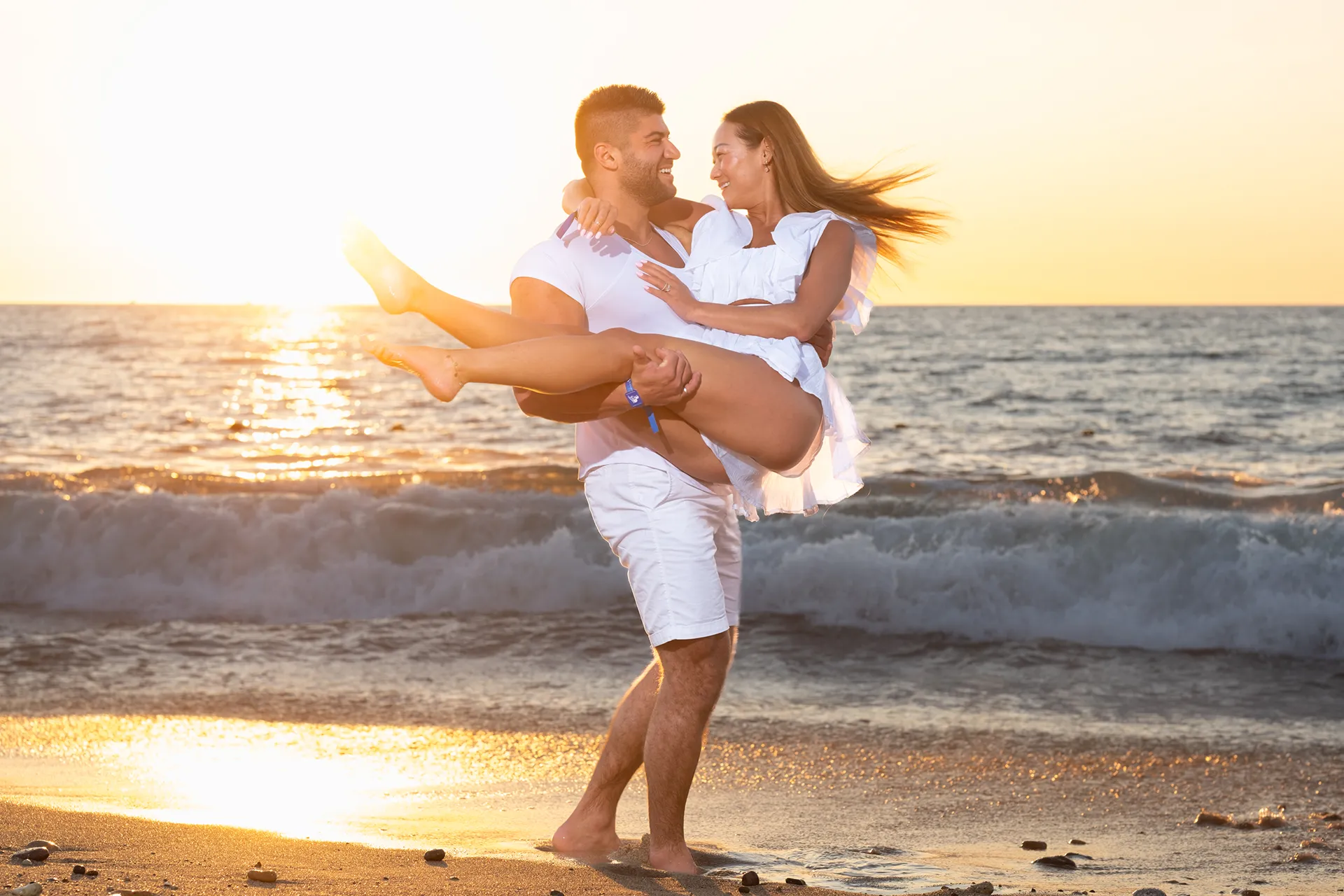 Man lifting his partner in his arms in the surf at sunset in Puerto Vallarta