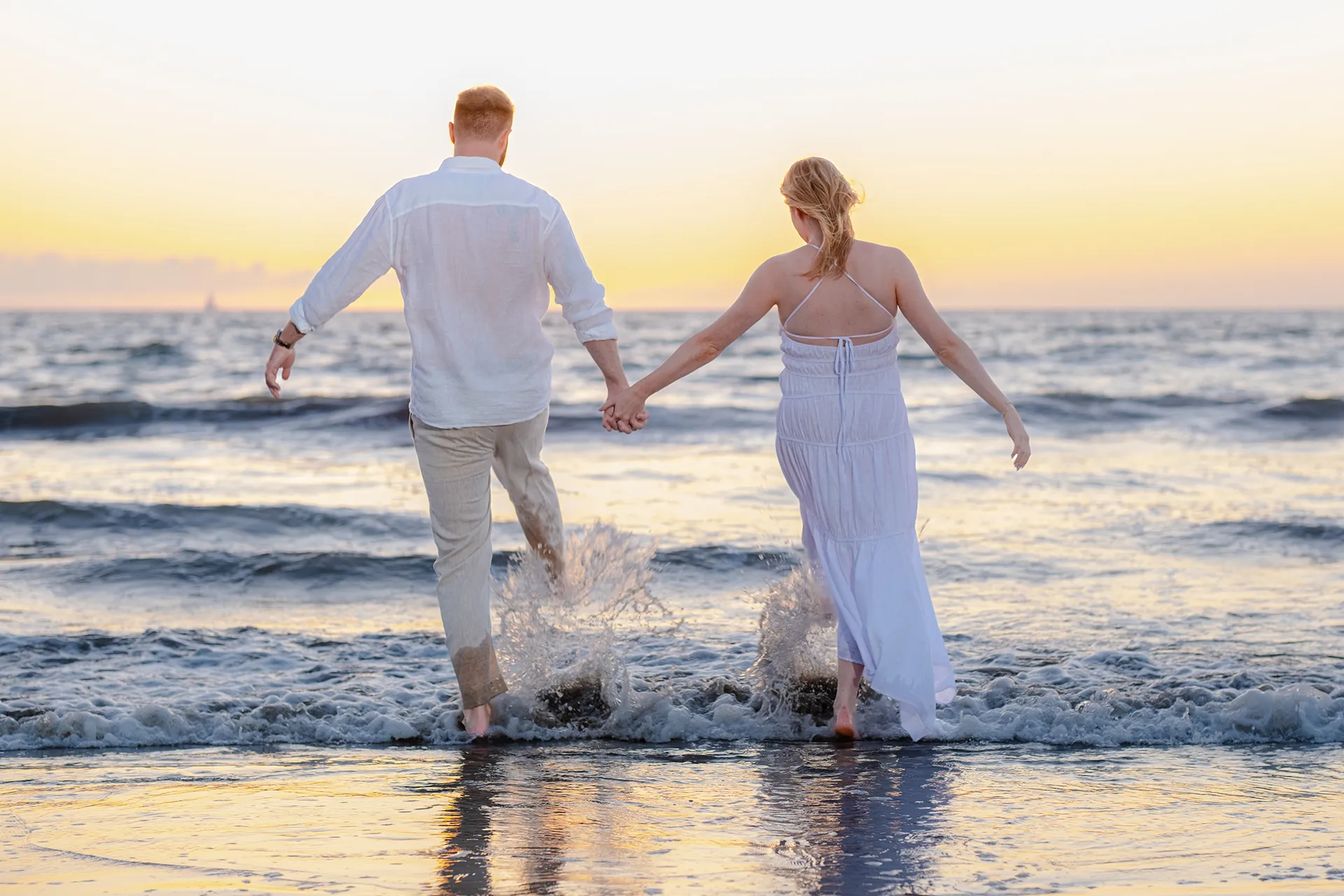 Couple walking hand in hand into the water, splashing through the shallows at sunset in Puerto Vallarta