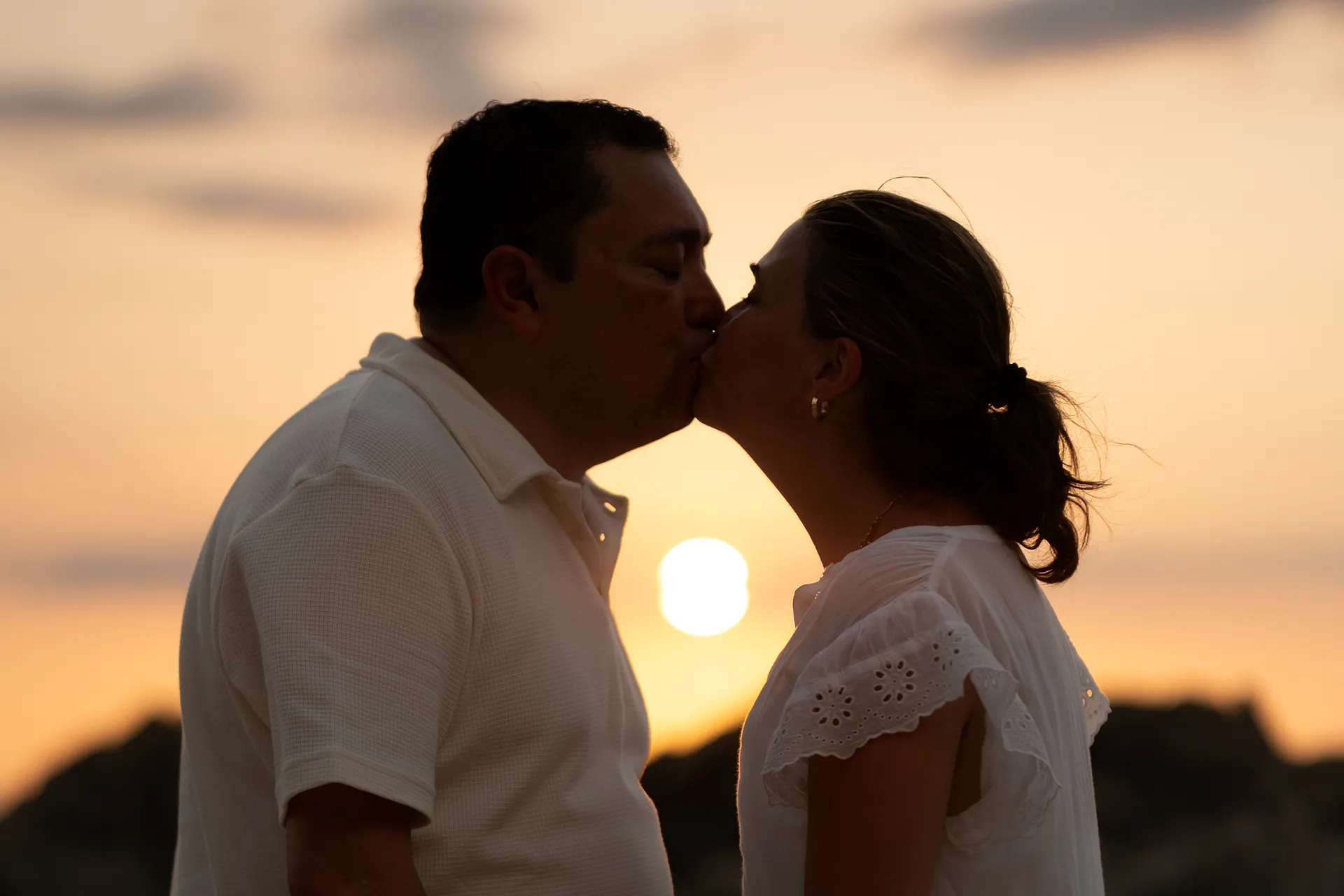 Couple kissing in silhouette with the setting sun framed between them on a Puerto Vallarta beach