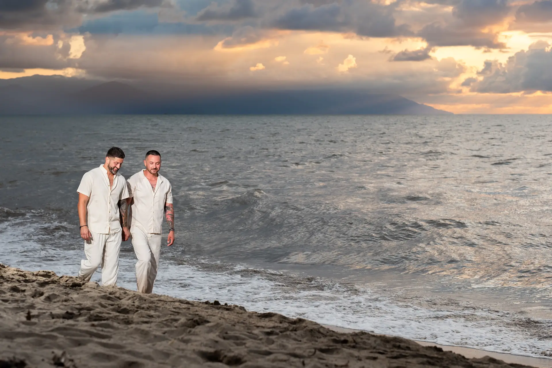 Two men walking together along the shoreline at dusk under a dramatic Puerto Vallarta sky