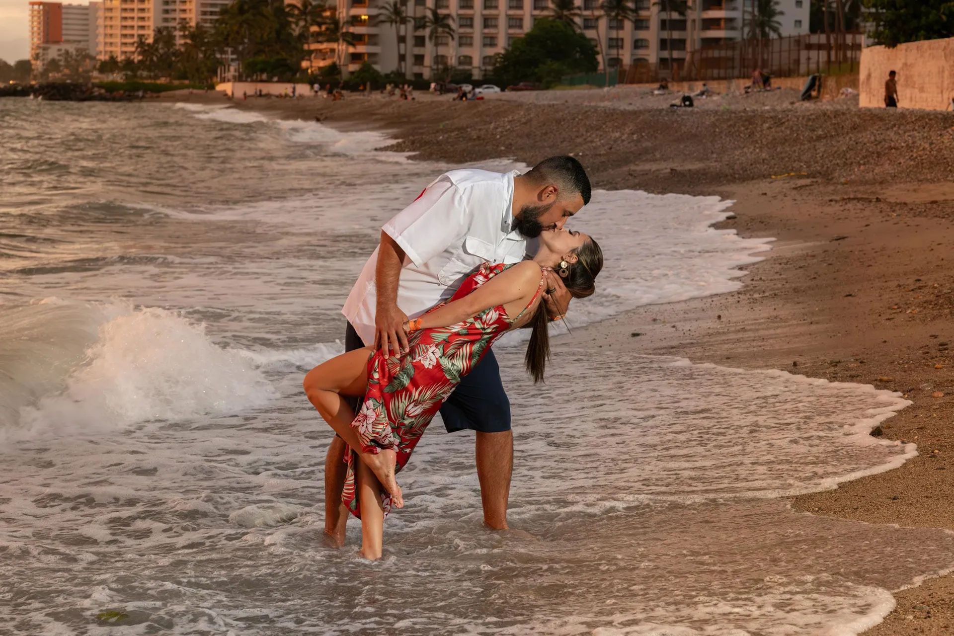 Couple sharing a dip and a kiss at the shoreline with the Puerto Vallarta hotel zone behind them