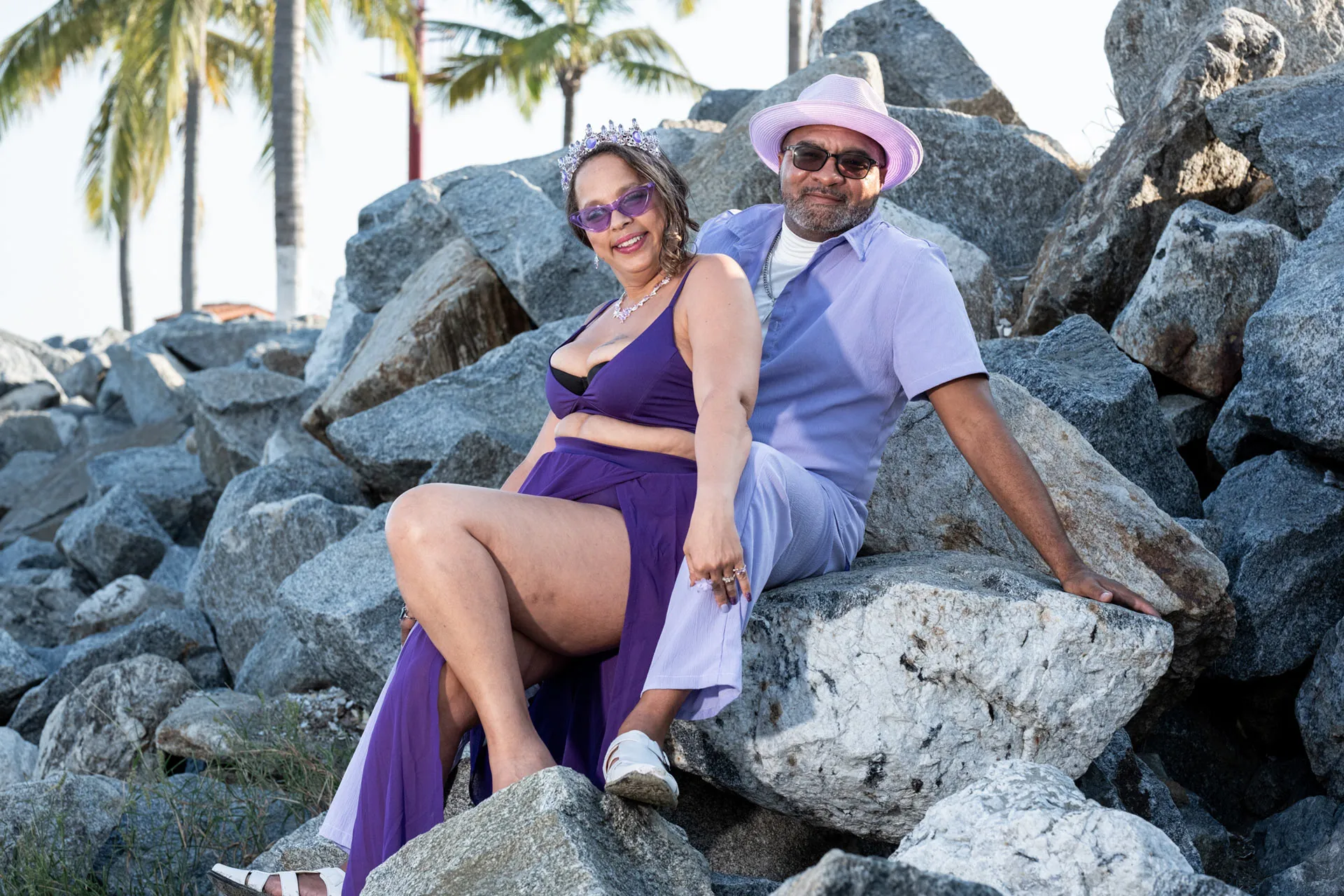 Couple seated together on the rocks in matching purple outfits with palm trees behind them in La Cruz de Huanacaxtle