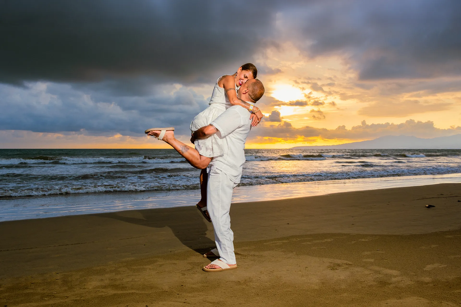 Couple in a dramatic dip pose against a cloudy sunset sky on the beach in Puerto Vallarta