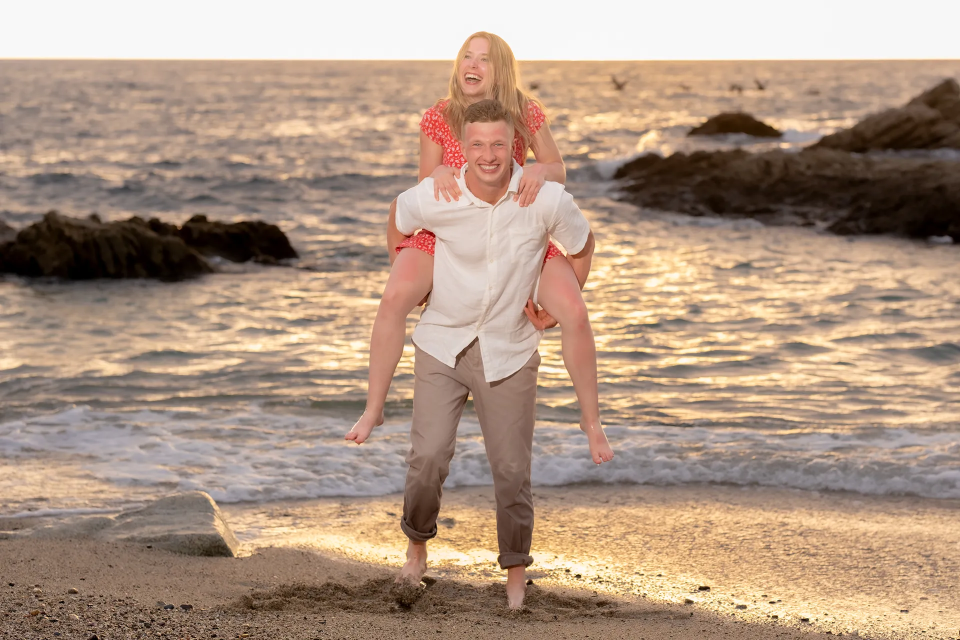 Couple laughing as he gives her a piggyback ride at the water's edge during a golden hour session in Puerto Vallarta