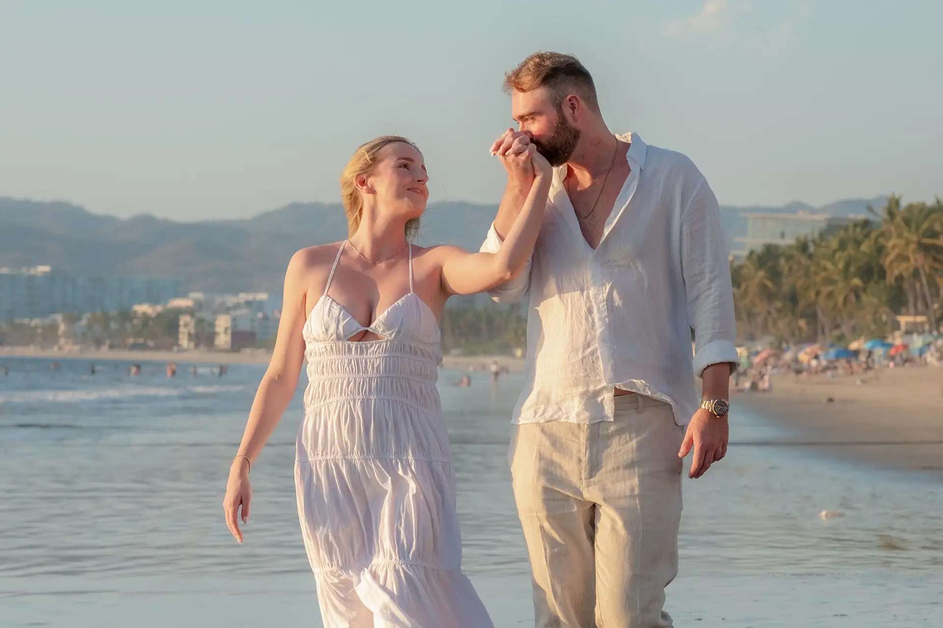 Man kissing his partner's hand as they walk along the shoreline at golden hour in Puerto Vallarta