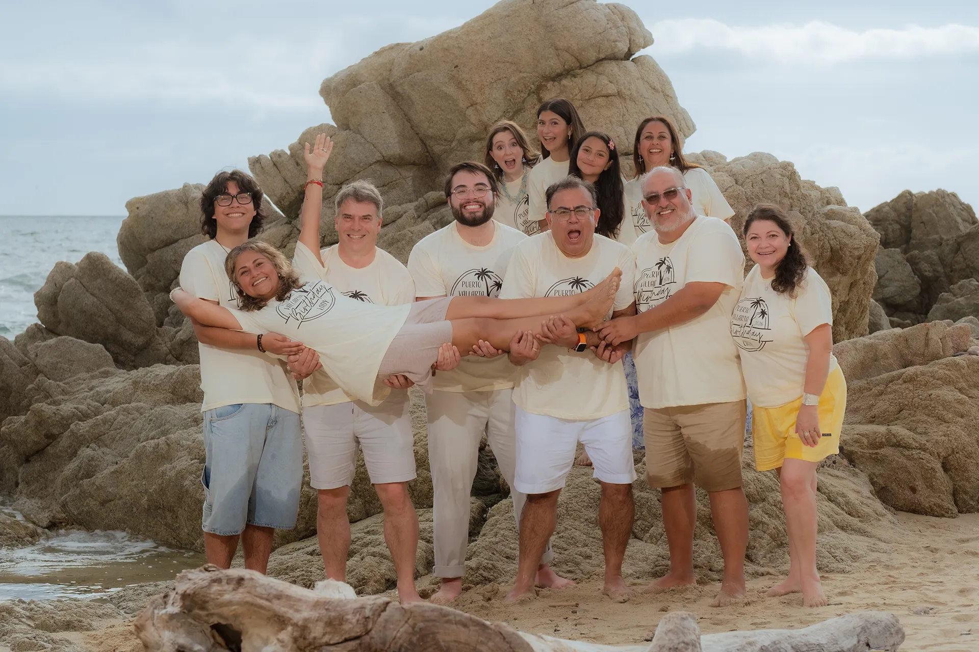 Family reunion group of eleven in matching shirts laughing together on the rocks in Conchas Chinas, Puerto Vallarta