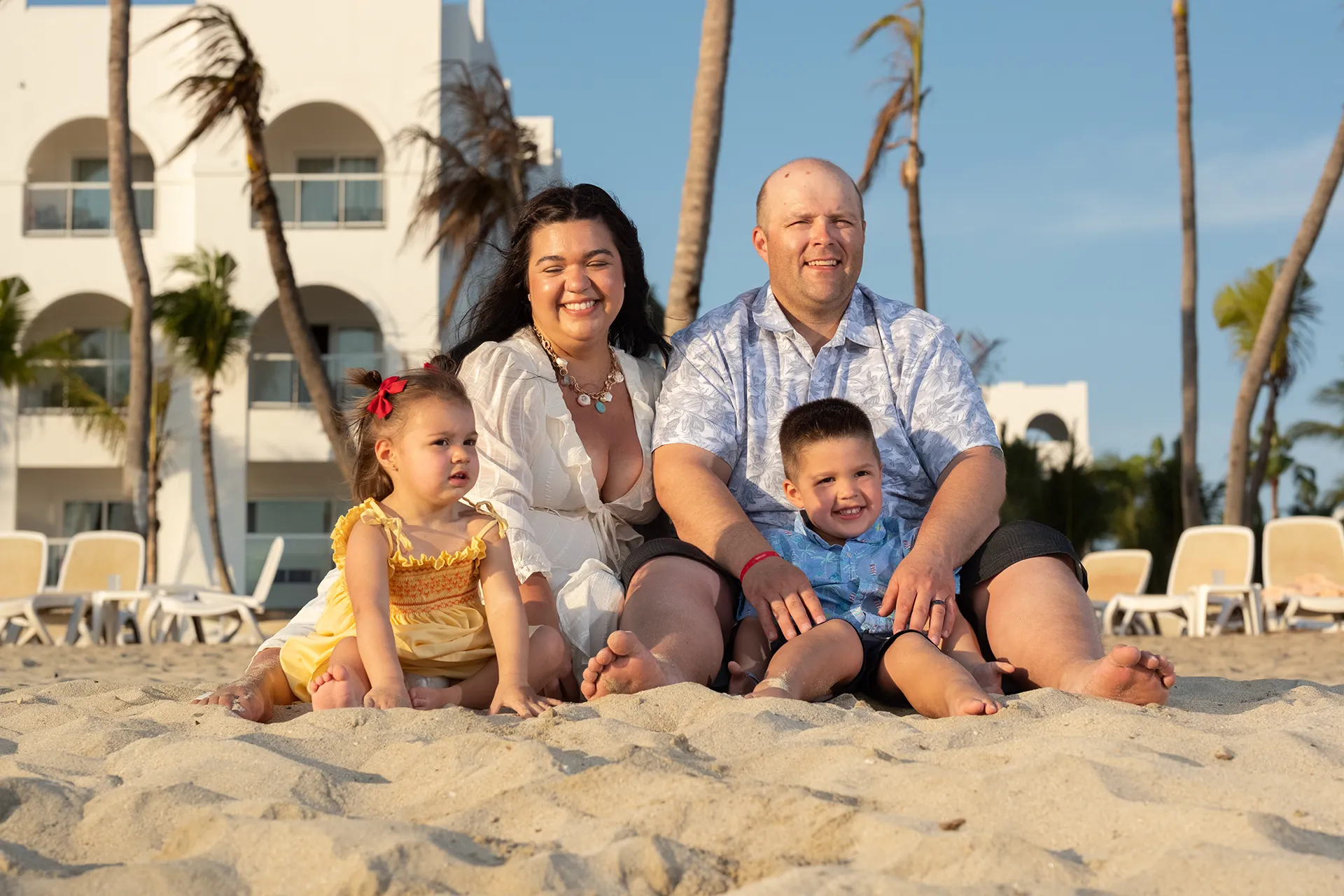 Family of four sitting together on the sand with their resort behind them in Nuevo Vallarta