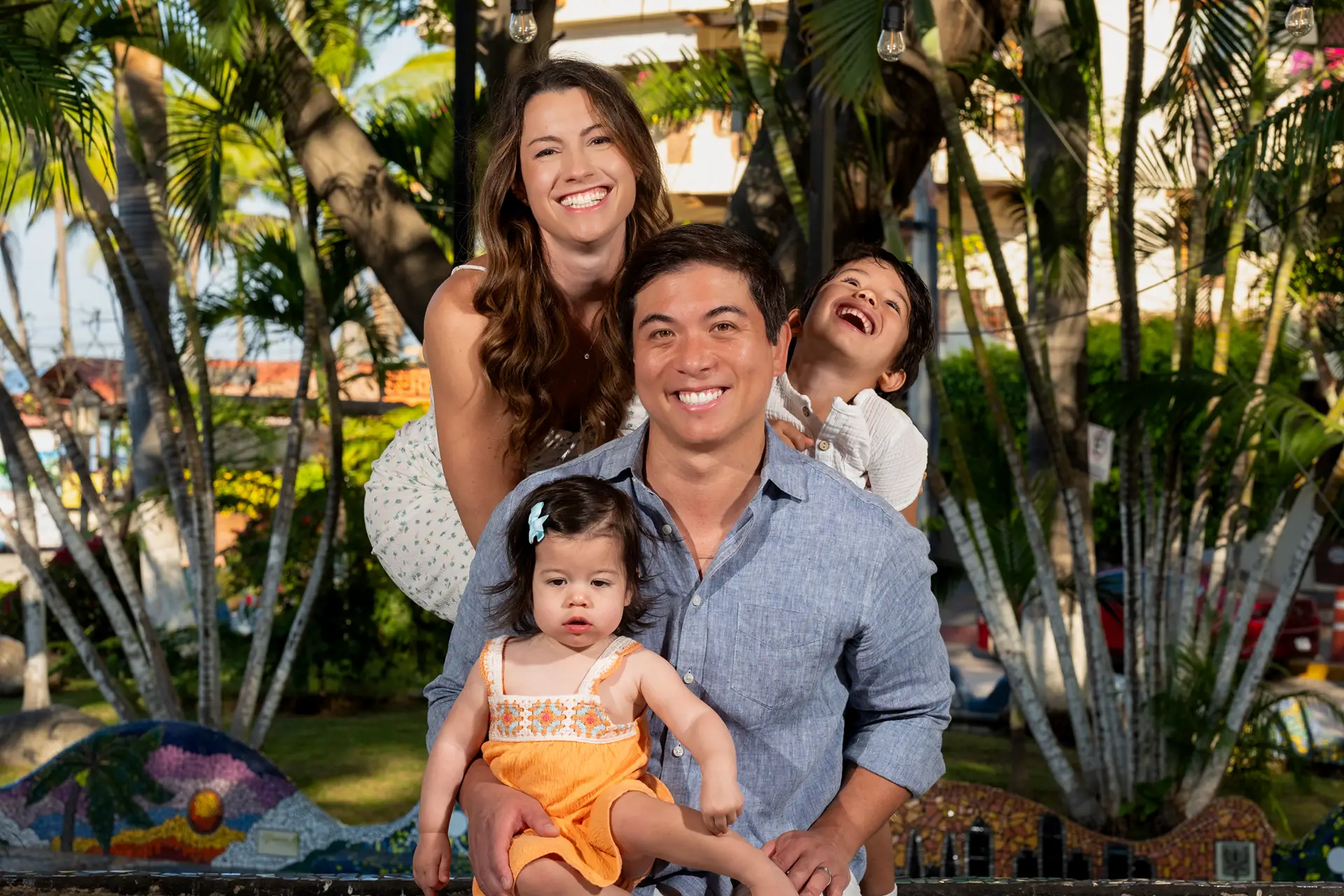 Parents and their two children laughing together under the palm trees during a family session in Puerto Vallarta