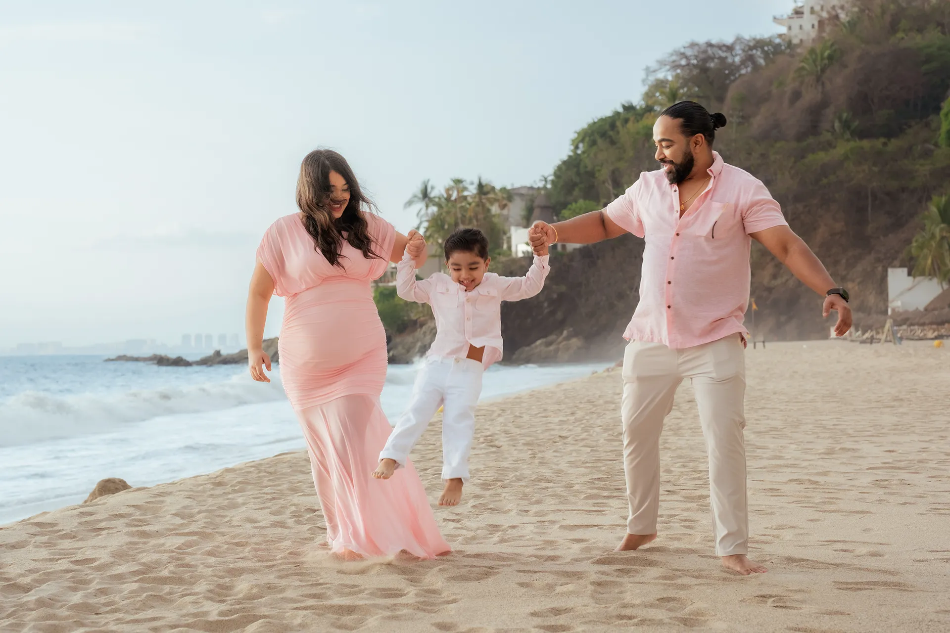 Expecting couple walking along the beach with their son between them in Puerto Vallarta