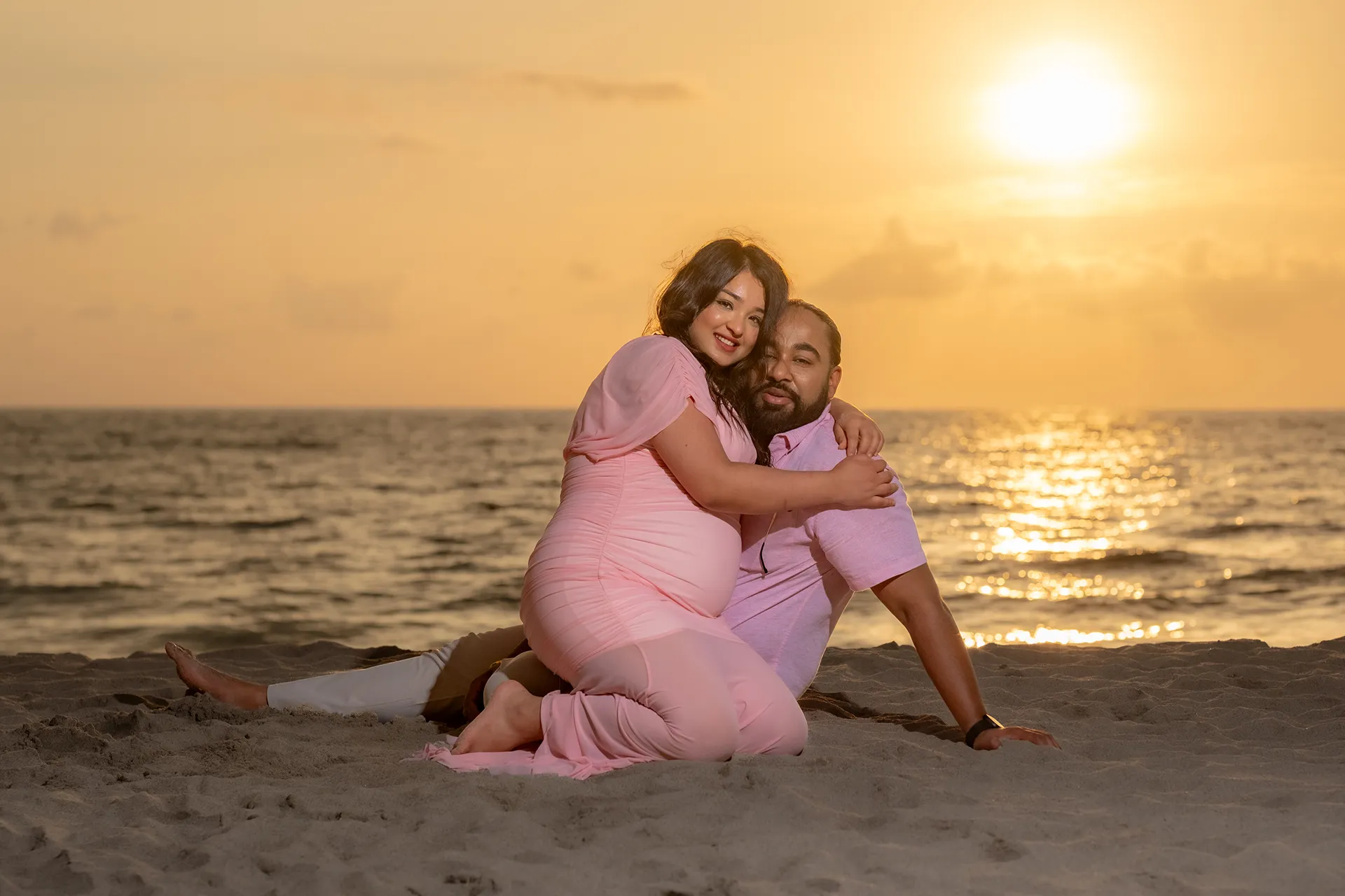 Expecting mother embracing her husband on the sand at sunset in Puerto Vallarta