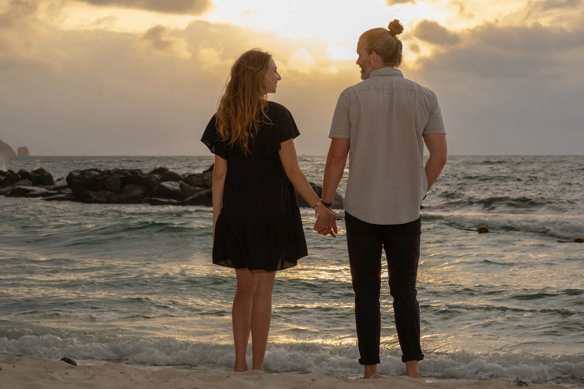 Expecting couple holding hands facing the ocean at sunset in Puerto Vallarta
