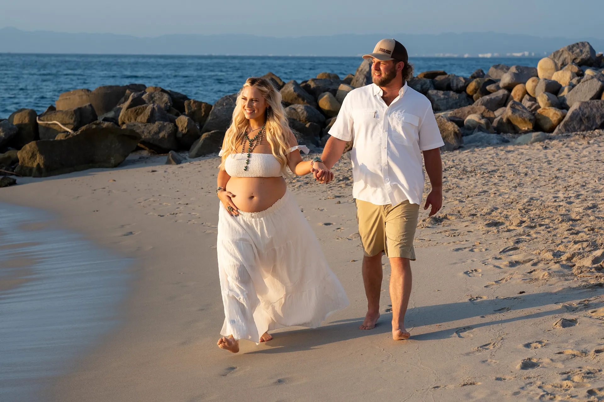 Expecting couple walking barefoot along the shoreline in Puerto Vallarta