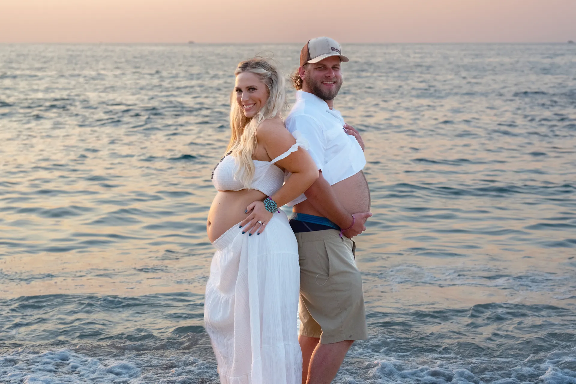 Expecting couple cradling the bump together in soft light on a Puerto Vallarta beach